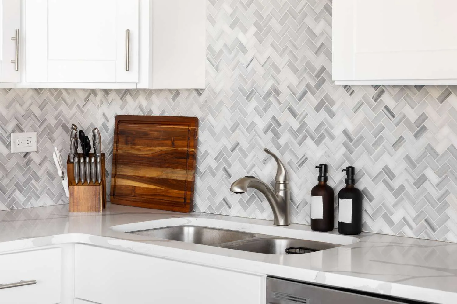 Herringbone marble mosaic backsplash detail above a kitchen counter and white cabinets