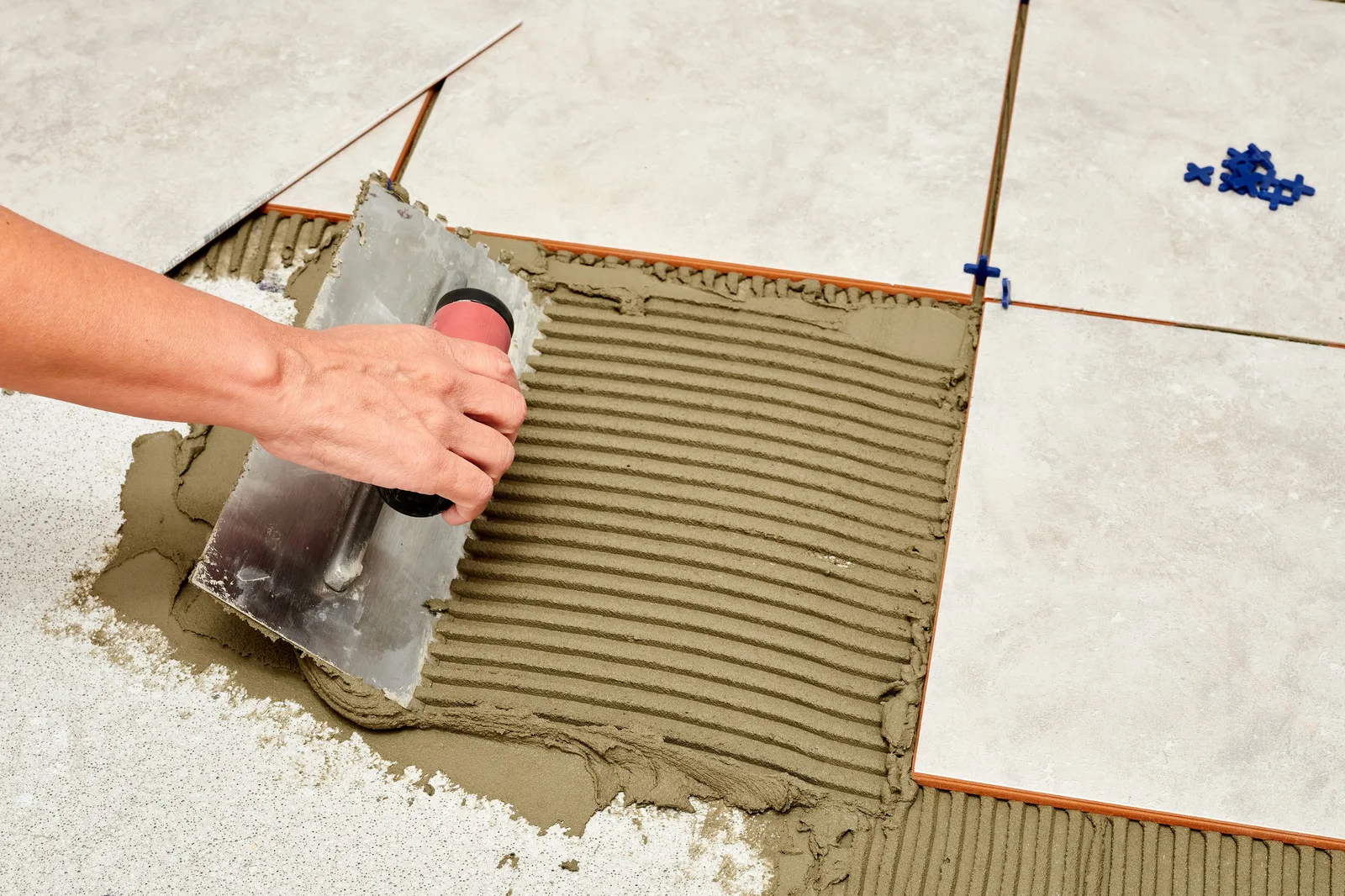 Floor tile being set into combed thinset with a notched trowel and blue tile spacers