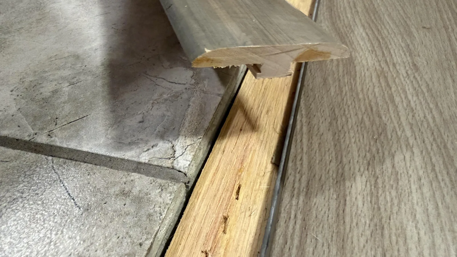 Wood transition strip fitted between an older tile floor and newly laid plank flooring