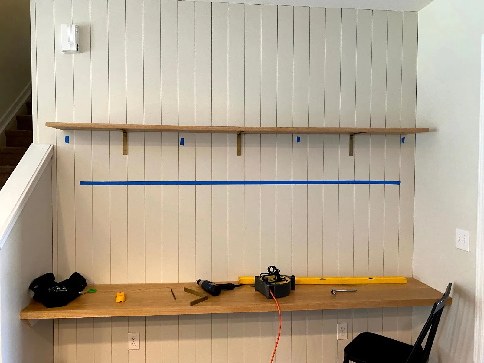 Wood shelves being mounted to a wall with a drill, a level and layout tape marking the line