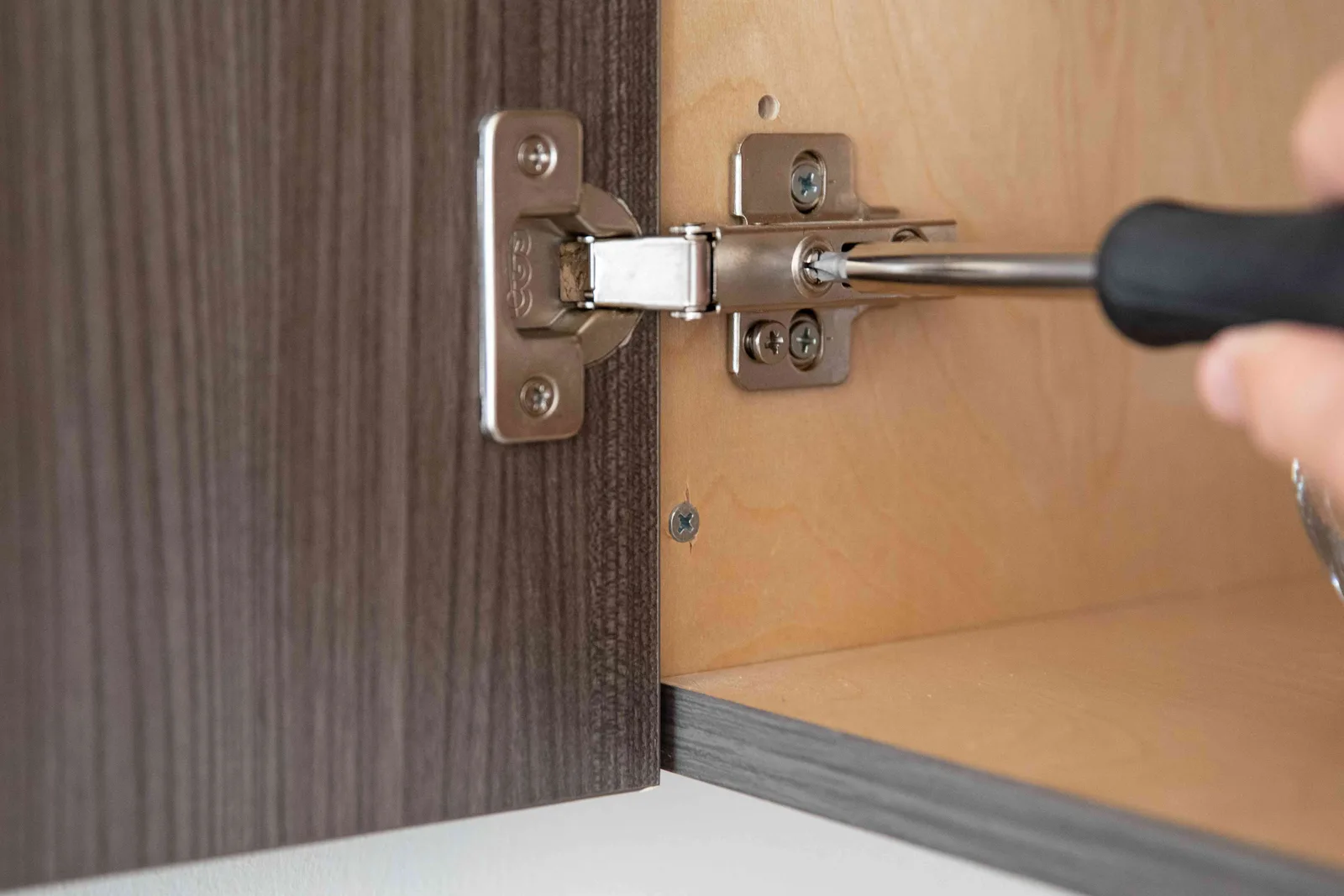 Screwdriver adjusting the hinge on a cabinet door