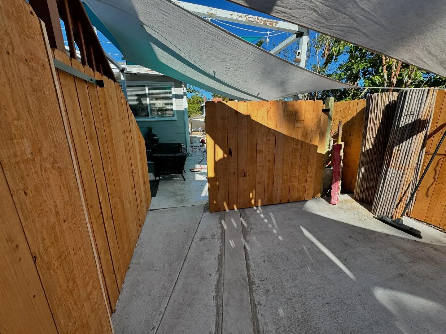 Wood privacy fence along a driveway with the sliding gate rolled open under shade sails