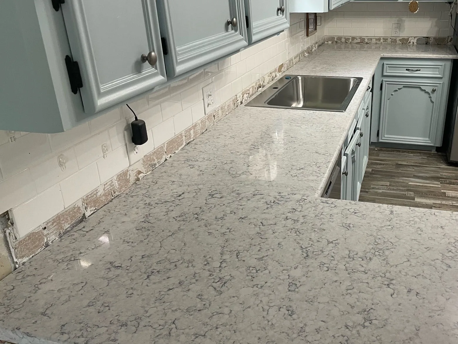 Newly installed quartz countertops on painted base cabinets with the old backsplash tile still torn out along the wall