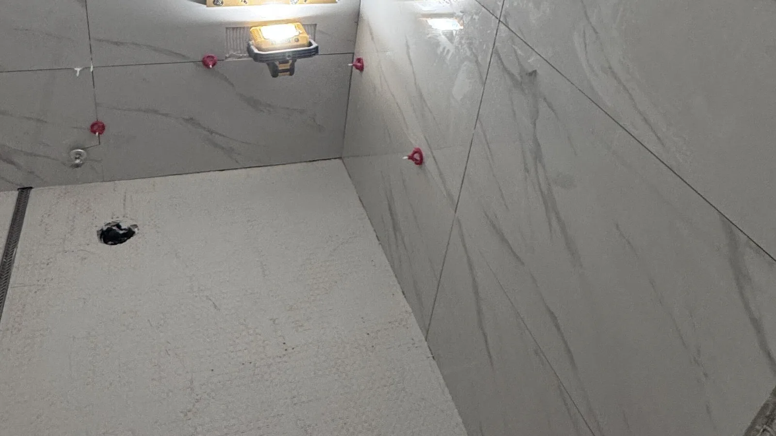 Large-format porcelain tile joints held by red leveling clips during a shower tile installation